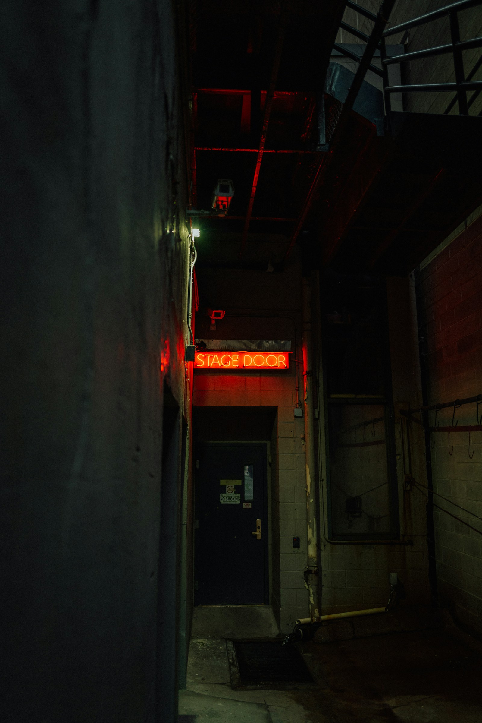 A red neon Stage Door sign above a doorway in a dark backstage passage